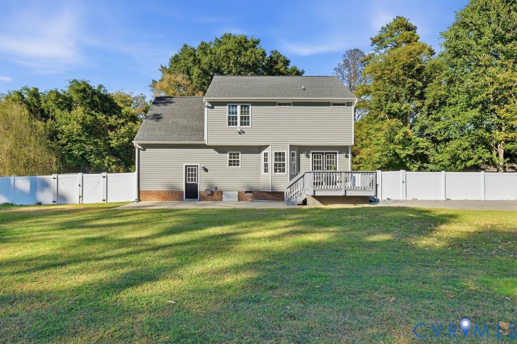 Two-story exterior featuring light gray vinyl siding, a brick water table, a raised wood deck, a rear concrete patio, and a fully fenced perimeter