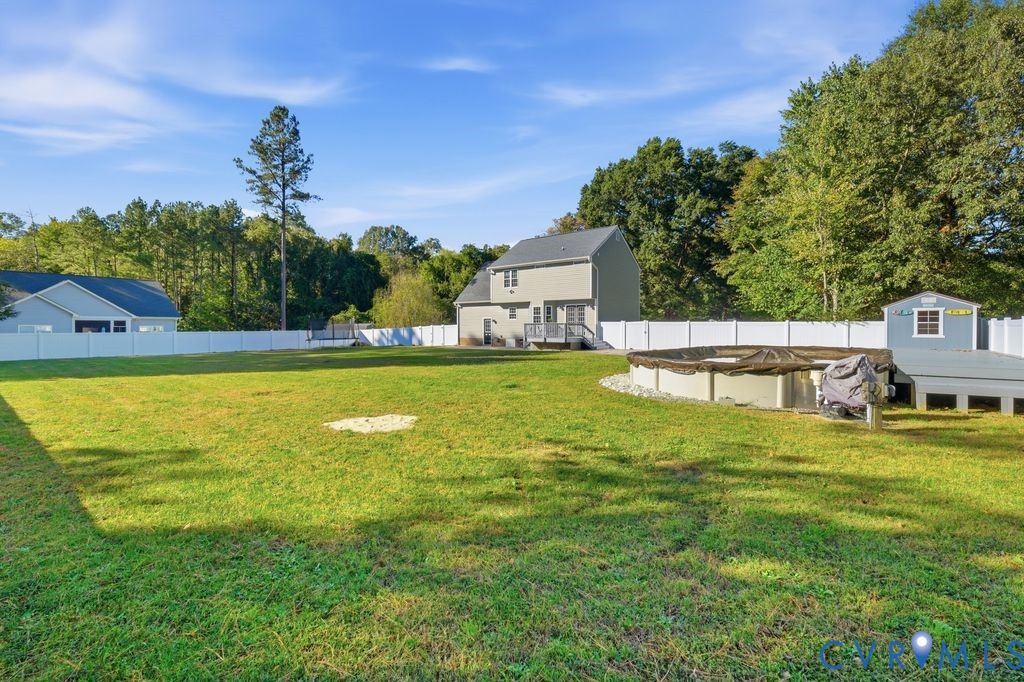 Expansive backyard featuring a vinyl privacy fence, an above-ground pool with a surrounding deck, and a detached storage structure