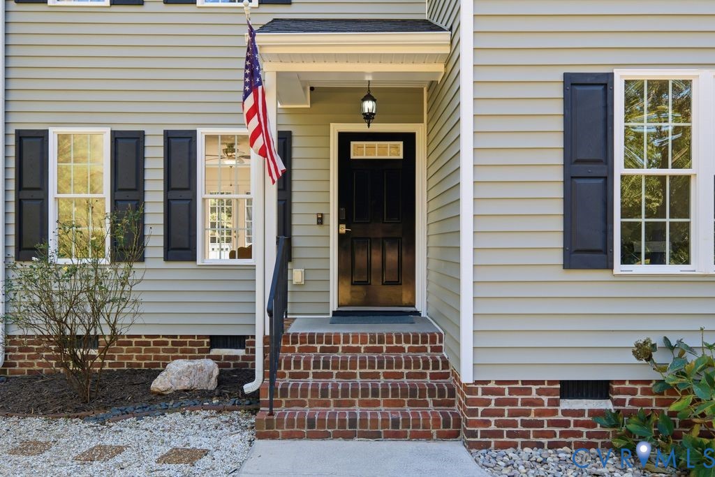 Traditional exterior featuring horizontal siding, dark shutters, a covered entryway with an attached exterior light fixture, multi-pane windows, and brick steps leading to a dark paneled front door