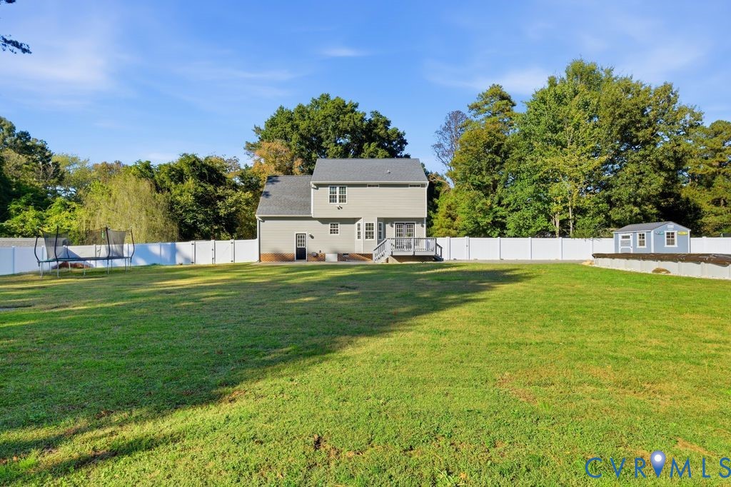 Expansive backyard featuring a large grass lawn, white vinyl fencing, a raised wooden deck, and a detached storage structure