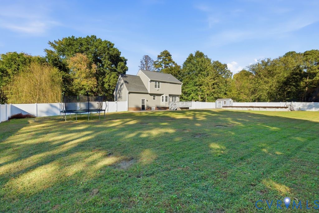 Expansive backyard featuring a large grass lawn, white vinyl fencing, and a detached storage shed