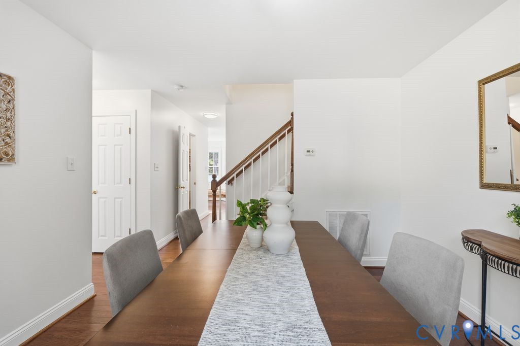 Dining area featuring wood-finish flooring, a staircase with a wooden handrail, and white vertical balusters