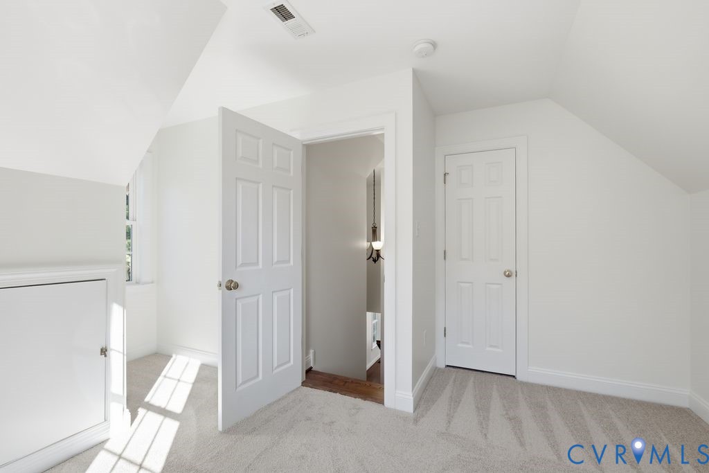 Room with neutral carpeting, vaulted ceilings, six-panel interior doors, and built-in knee-wall storage