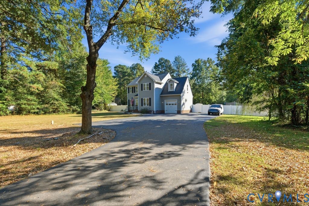 Two-story exterior featuring light-toned siding, asphalt driveway, single-car attached garage, and surrounding mature trees on a spacious lot