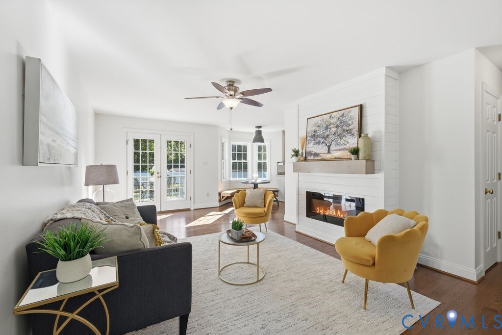 Spacious interior featuring a white shiplap fireplace surround, wooden mantel, wood-finish flooring, double glass-paneled exterior doors, and a ceiling fan