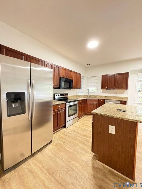 Kitchen featuring wood cabinetry, stone countertops, central island, stainless steel refrigerator, and integrated stainless steel oven and microwave Kitchen featuring wood cabinetry, stone countertops, central island, stainless steel refrigerator, and integrated stainless steel oven and microwave