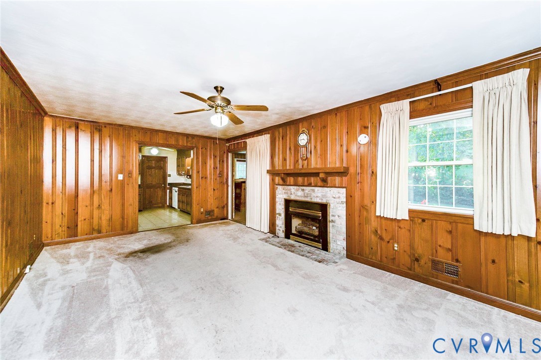 Living area featuring wood paneling, a fireplace with a light-toned masonry surround, a wooden mantel, and a ceiling-mounted light fixture with a fan