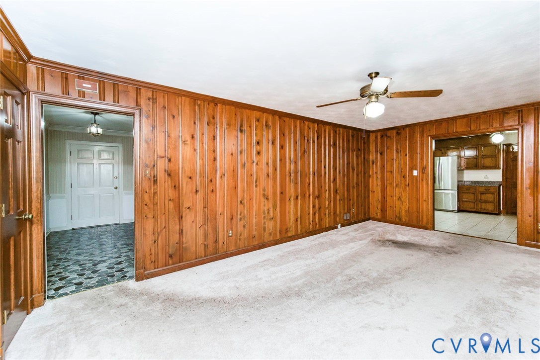 Interior space featuring wood paneling, a ceiling fan with integrated lighting, and wall-to-wall carpeting