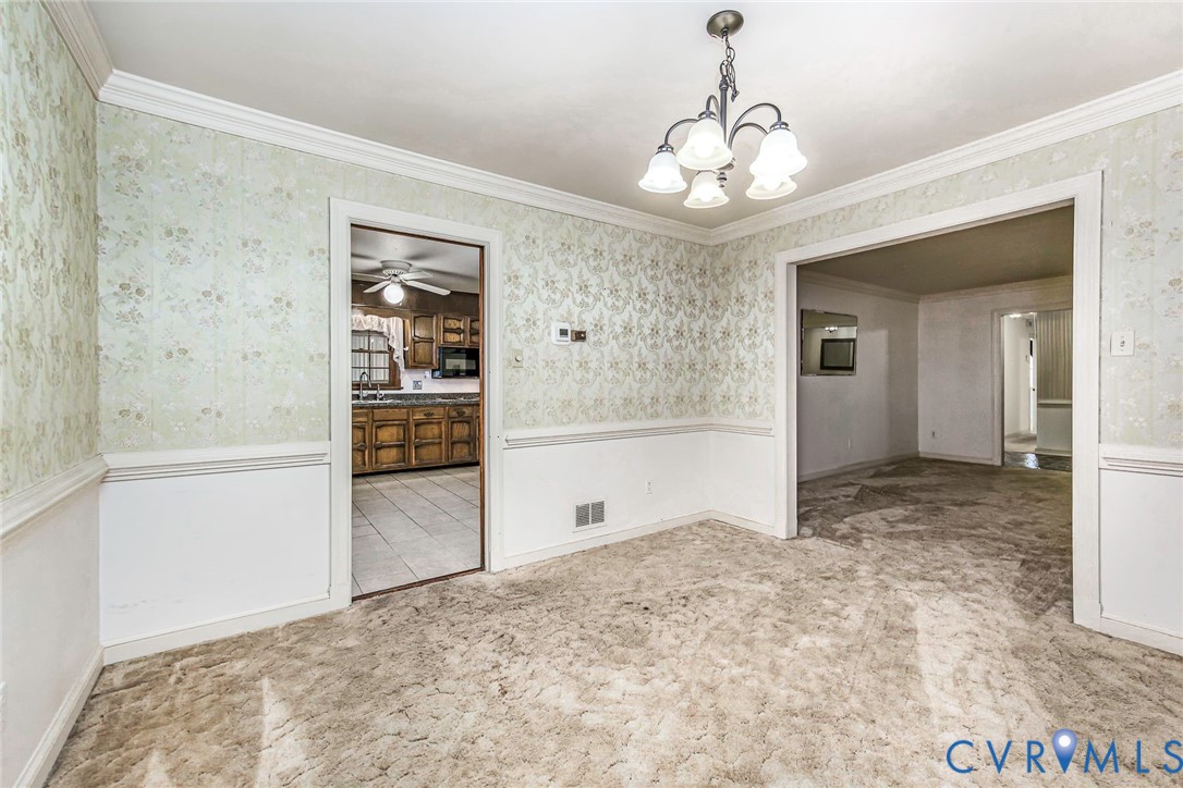 Formal dining area featuring crown molding, chair rail millwork, wallpapered walls, and a multi-arm overhead light fixture