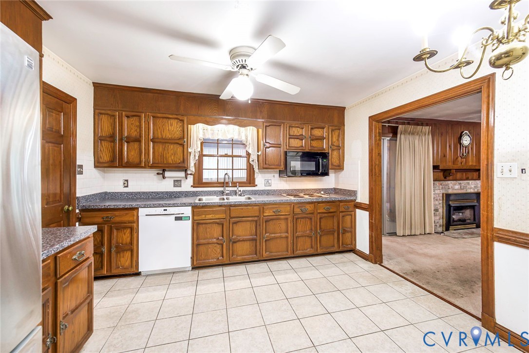 Kitchen featuring stained wood cabinetry, stone-finish countertops, ceramic tile flooring, a built-in microwave, and a ceiling fan with integrated lighting