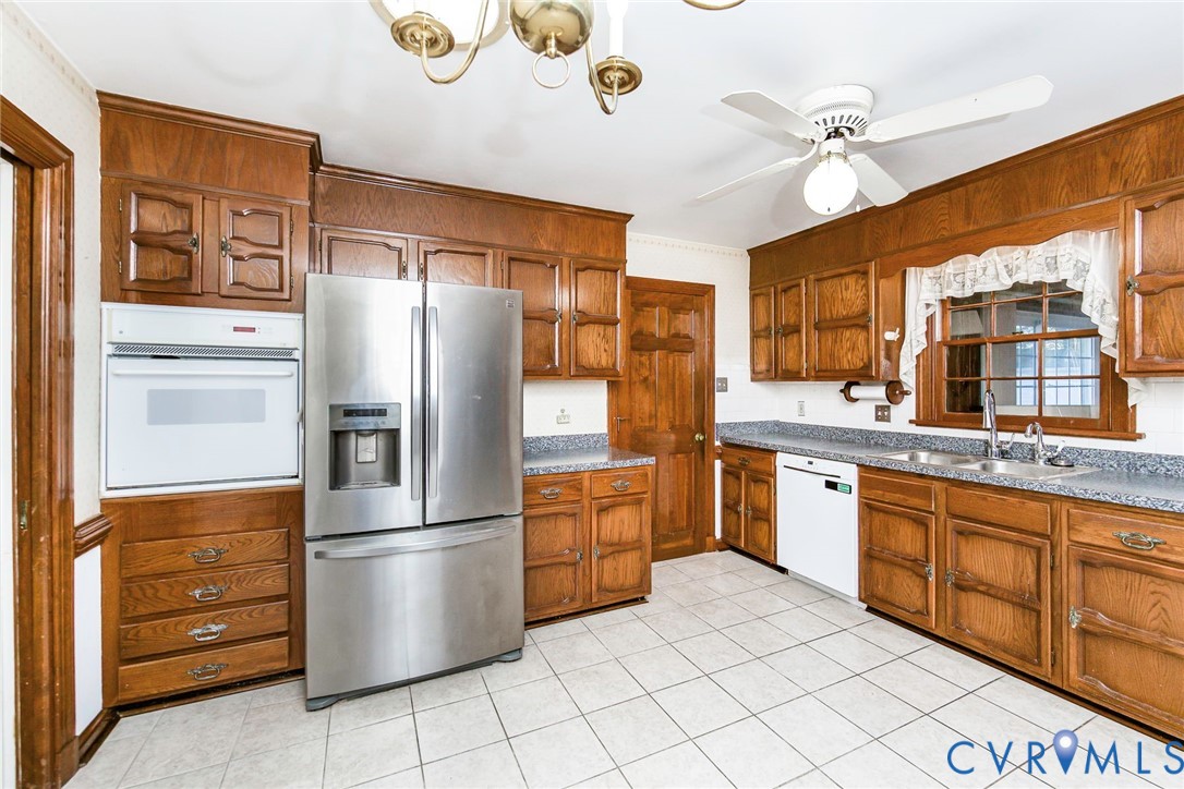 Kitchen featuring raised-panel oak cabinetry, speckled stone-composite countertops, stainless steel refrigerator, built-in wall oven, and ceramic tile flooring
