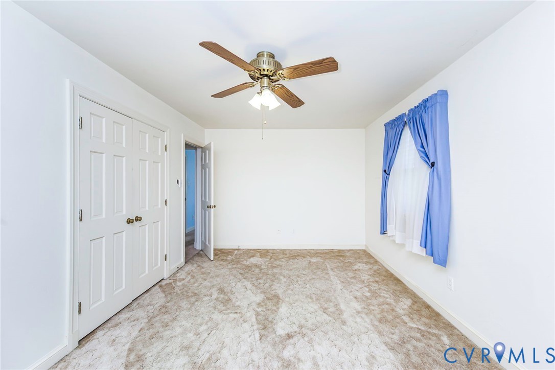 Neutral-toned carpeted flooring, multi-panel closet doors, and a ceiling-mounted fan with integrated lighting