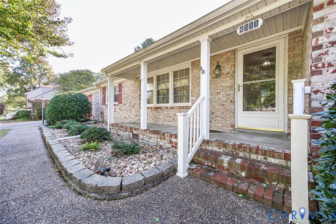 Brick exterior facade featuring a covered front porch, stone-retained landscaping bed, multi-pane windows with shutters, and concrete walkway Brick exterior facade featuring a covered front porch, stone-retained landscaping bed, multi-pane windows with shutters, and concrete walkway
