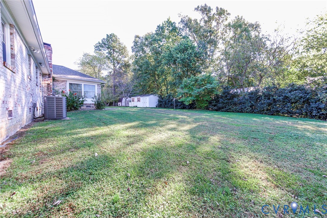 Expansive backyard featuring a brick exterior facade, mature trees, dense hedge landscaping, and a detached storage shed