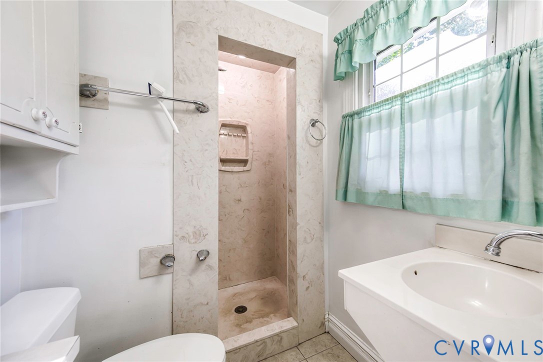 Walk-in shower featuring stone-tiled surround and built-in recessed niche, pedestal sink with integrated faucet, and custom-fit built-in cabinetry