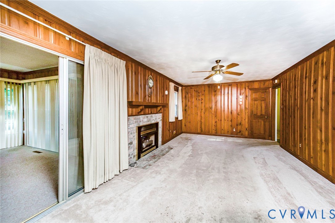 Wood-paneled walls, brick fireplace with a wood mantel, sliding glass door, and a ceiling fan with integrated lighting