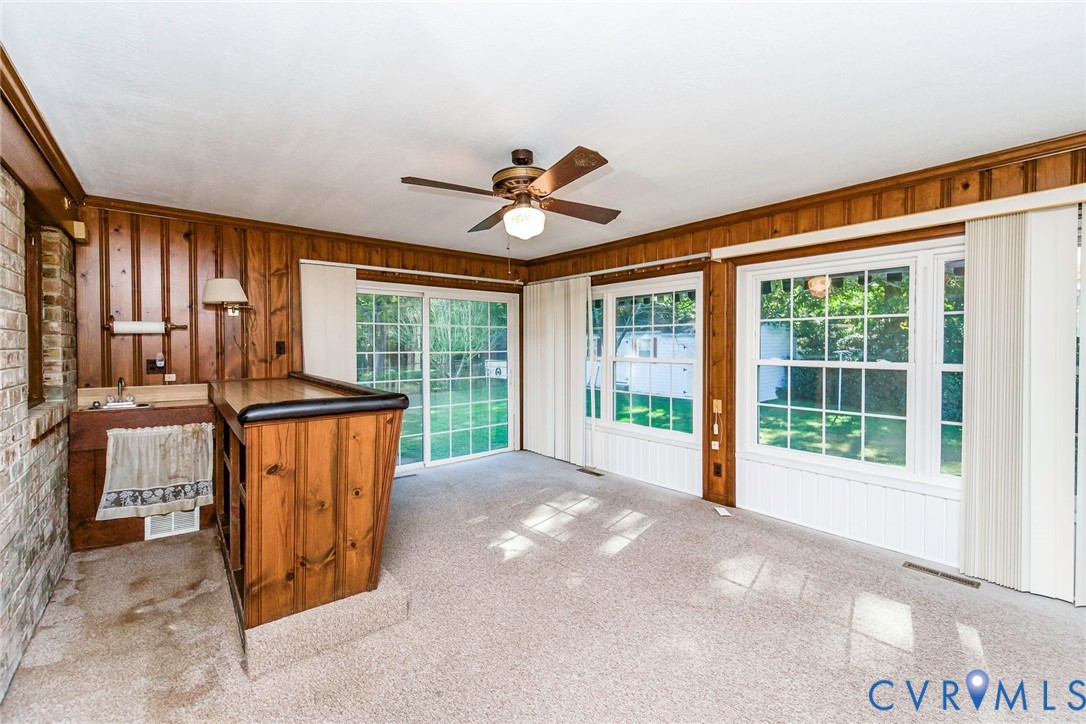 Wood-paneled room featuring a built-in wet bar, large windows with white trim, a ceiling fan, and sliding glass doors
