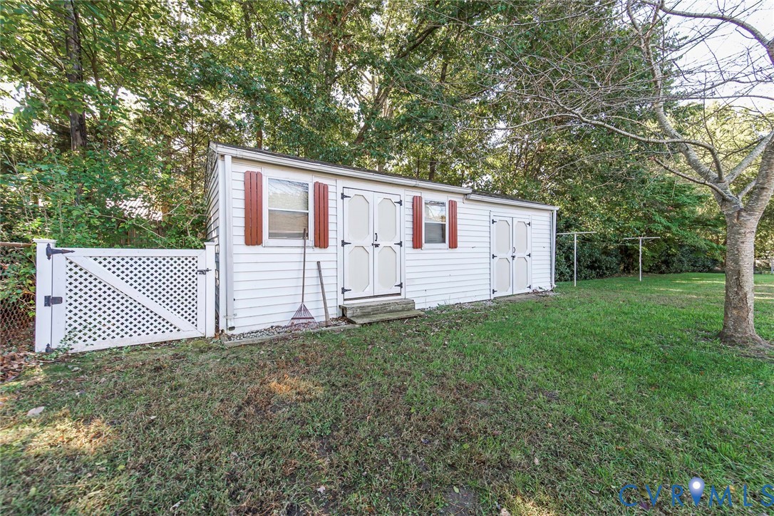 Storage structure featuring white horizontal siding, dual entrance doors, and decorative shutters, complemented by a white lattice fence
