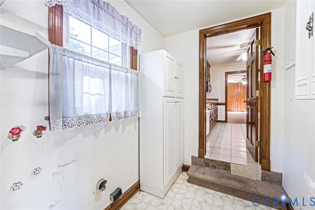 Utility area featuring built-in white cabinetry, multi-pane window with wood trim, and tile flooring