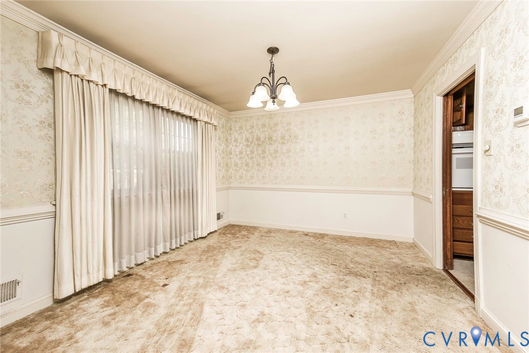 Room featuring decorative wallpaper, crown molding, chair rail trim, and a multi-arm chandelier Room featuring decorative wallpaper, crown molding, chair rail trim, and a multi-arm chandelier