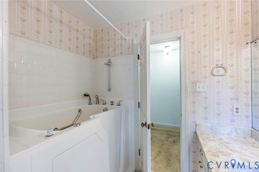 Step-in bathtub with integrated grab bars, white subway tile surround, laminate countertop, and wallpapered walls