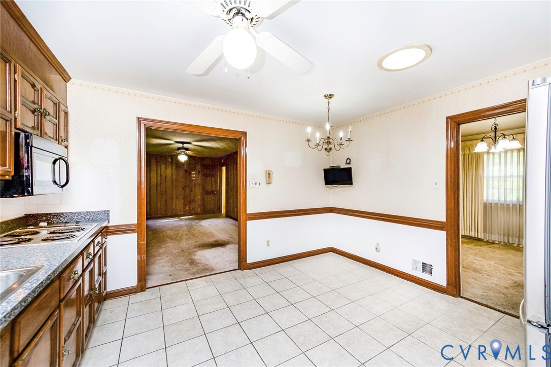 Kitchen area featuring square tile flooring, wood-toned cabinetry, a built-in microwave, a ceiling fan with integrated lighting, and a multi-arm chandelier