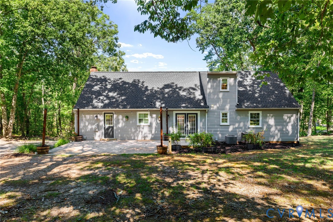 Two-story residence featuring light-colored horizontal siding, asphalt shingle roofing, a paved patio, and double glass-paneled exterior doors