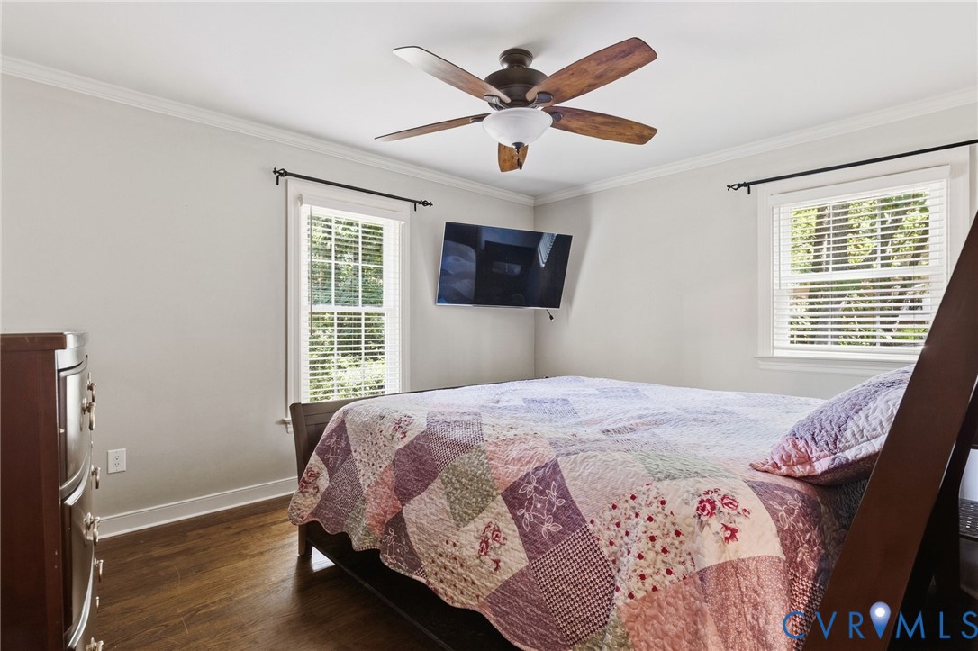 Room featuring wood-finish flooring, crown molding, double-hung windows with integrated blinds, and a central ceiling fan with integrated lighting