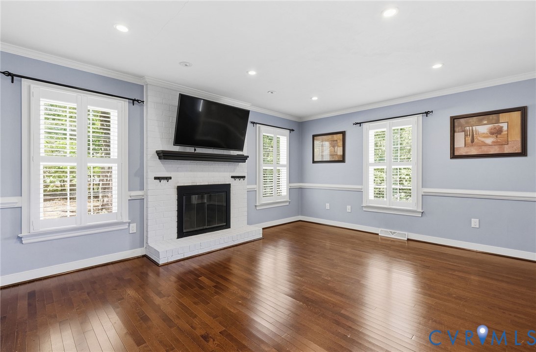 Brick fireplace with a dark mantle, wood-finish flooring, recessed lighting, and white plantation shutters