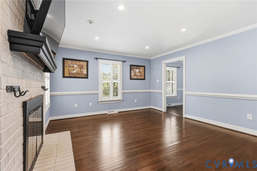 Brick fireplace with a mantel, wood-finish flooring, recessed lighting, crown molding, and chair rail wainscoting