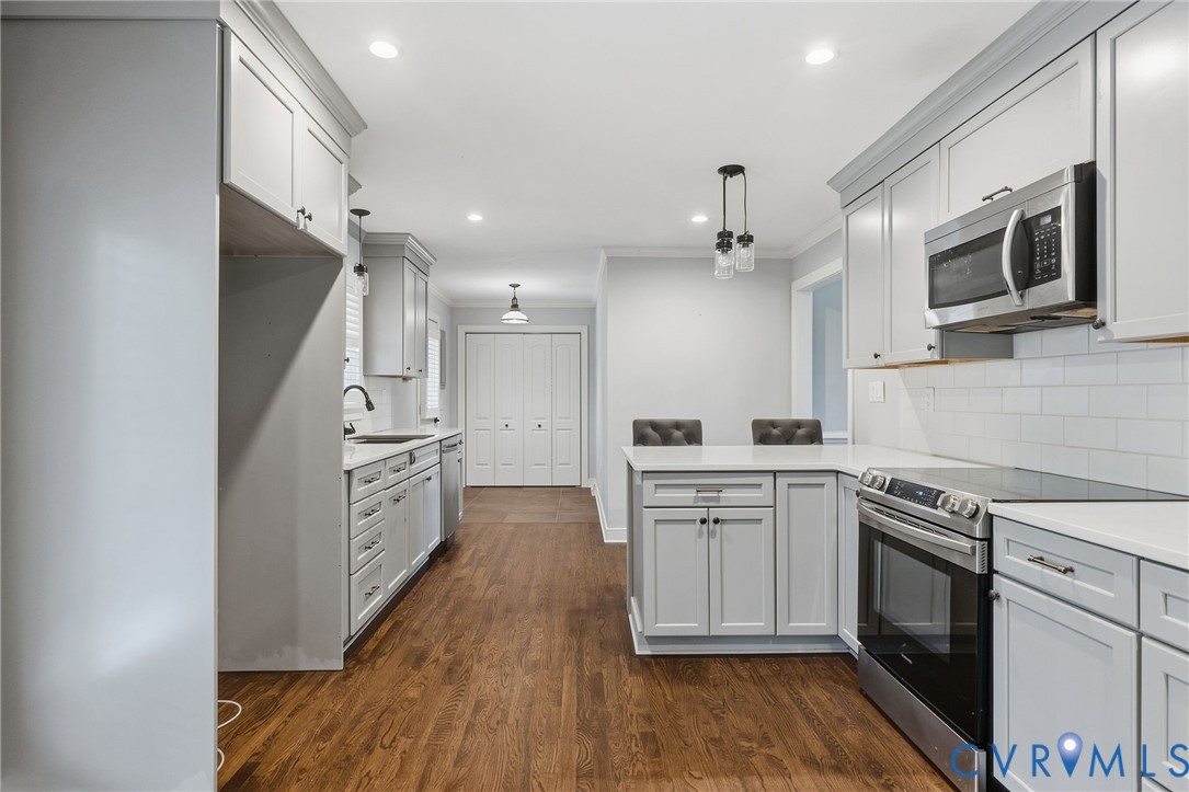 Kitchen featuring shaker-style cabinetry, quartz countertops, subway tile backsplash, stainless steel appliances, and wood-finish flooring