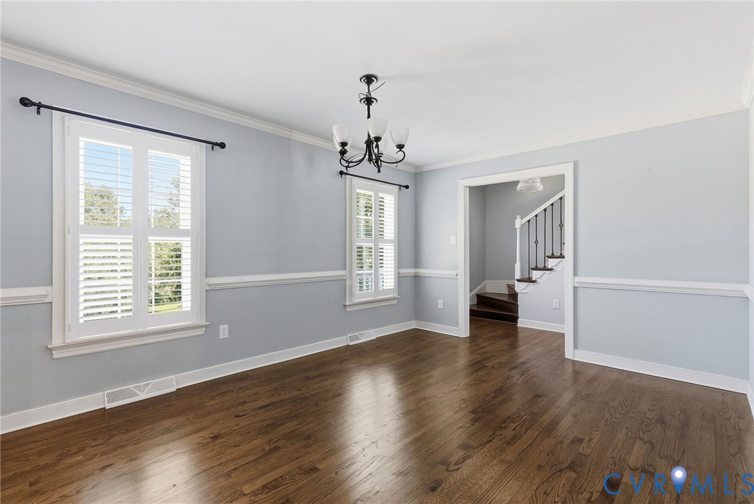 Room featuring wood-finish flooring, white plantation shutters, chair rail molding, and a central multi-arm chandelier