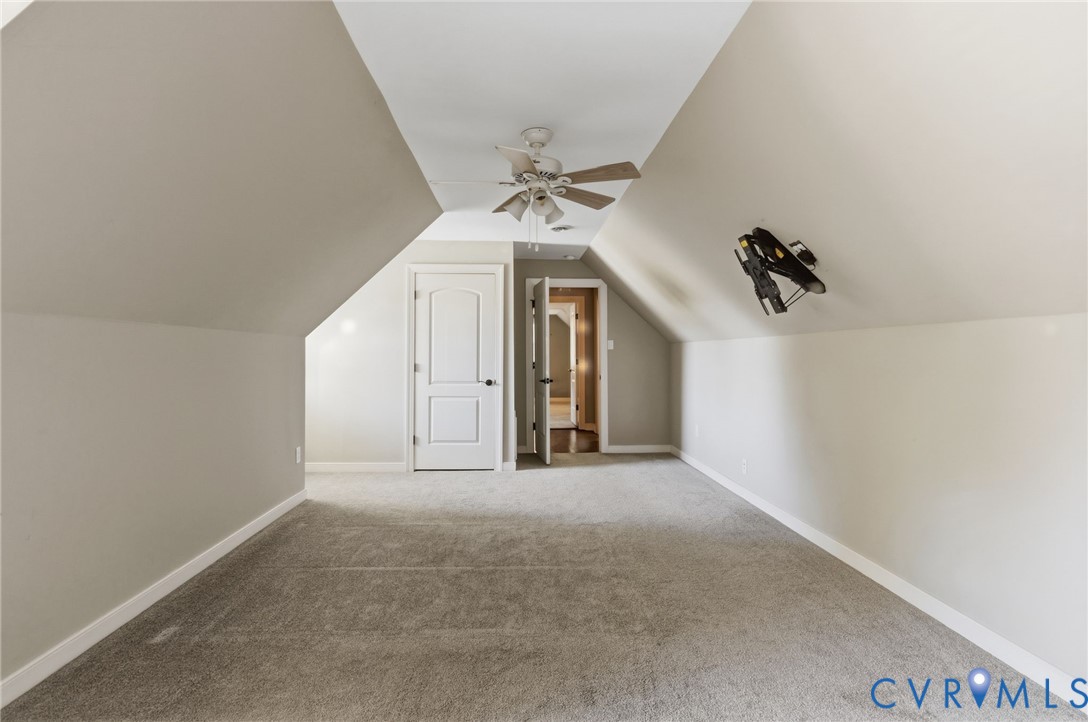 Vaulted ceiling featuring a central white ceiling fan with integrated lighting, wall-to-wall carpeting, and a multi-panel interior door