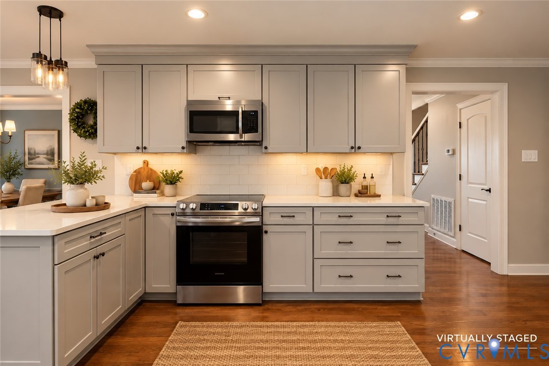 Kitchen featuring light gray shaker-style cabinetry, white subway tile backsplash, stainless steel appliances, light-toned solid surface countertops, and wood-finish flooring