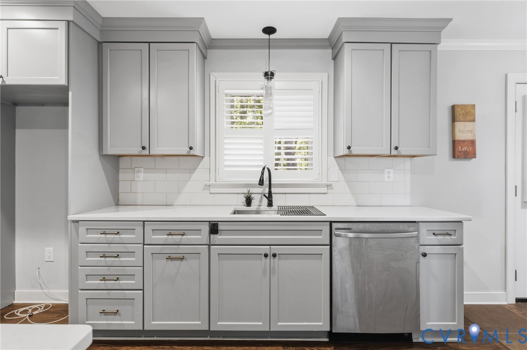 Kitchen featuring shaker-style cabinetry with crown molding, white subway tile backsplash, solid-surface countertops, undermount stainless steel sink with matte black pull-down faucet, and plantation shutters