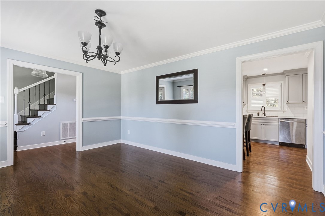 Dining area featuring dark wood-finish flooring, chair rail molding, crown molding, and a multi-arm chandelier
