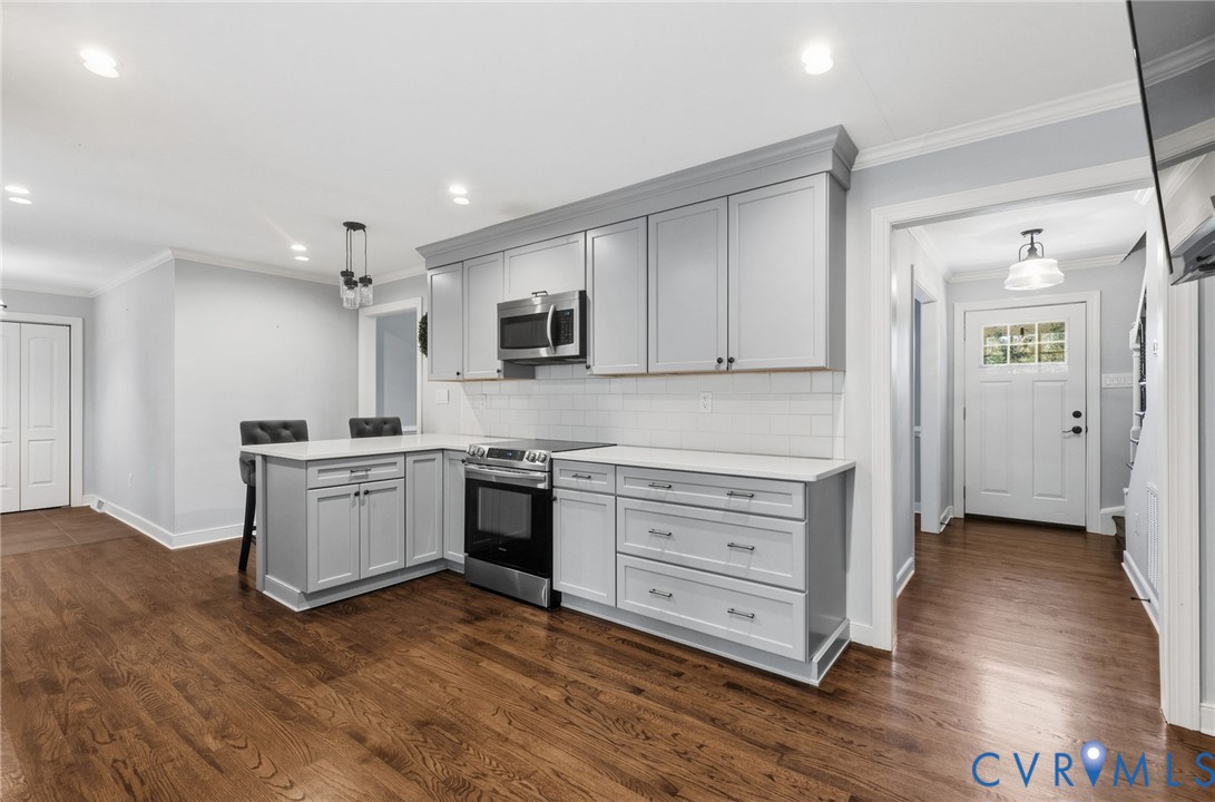 Kitchen featuring light gray cabinetry, solid-surface countertops, subway tile backsplash, stainless steel appliances, and wood-finish flooring