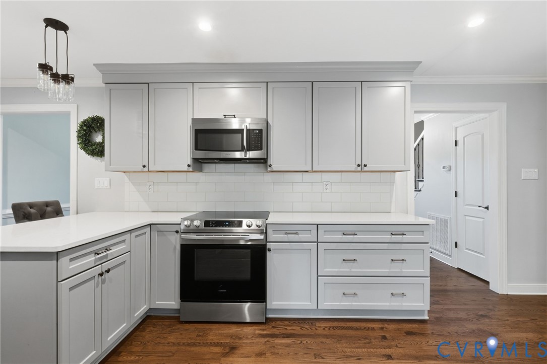 Kitchen featuring light-gray shaker-style cabinetry, quartz countertops, white subway tile backsplash, stainless steel appliances, and wood-finish flooring
