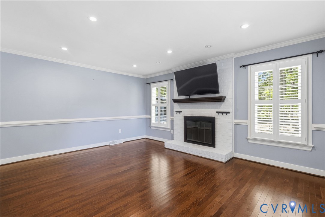 Living area featuring wood-finish flooring, recessed lighting, crown molding, chair rail trim, and a white brick fireplace with a wood mantel