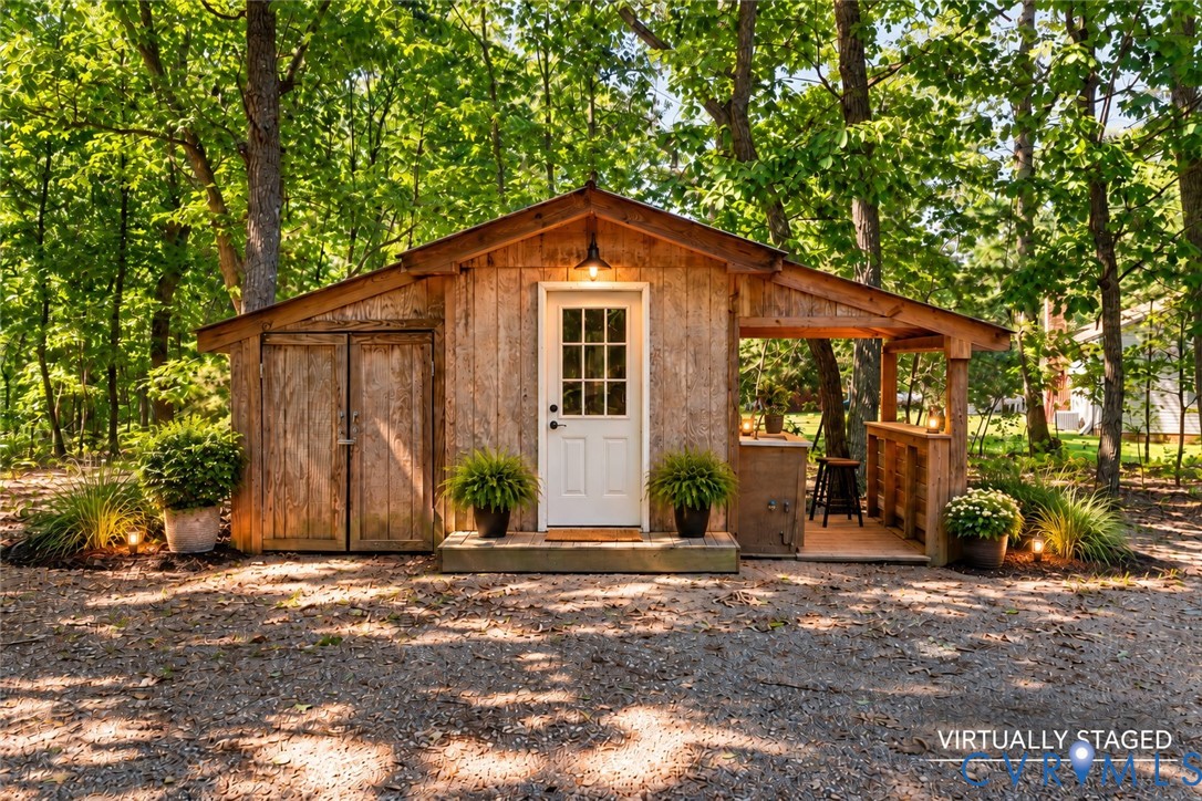 Rustic wood-sided outbuilding featuring a covered porch, built-in wooden bar, double-door storage access, and exterior wall-mounted lighting