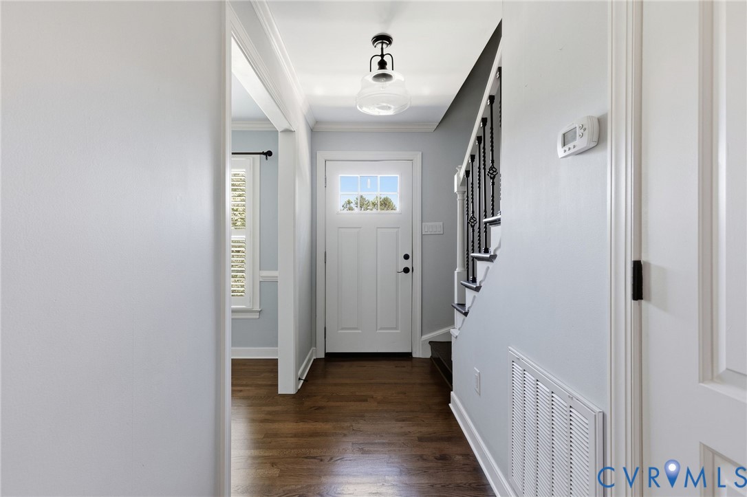 Foyer featuring wood-finish flooring, a decorative pendant light fixture, a paneled entry door with a glass inlay, and a staircase with metal spindles