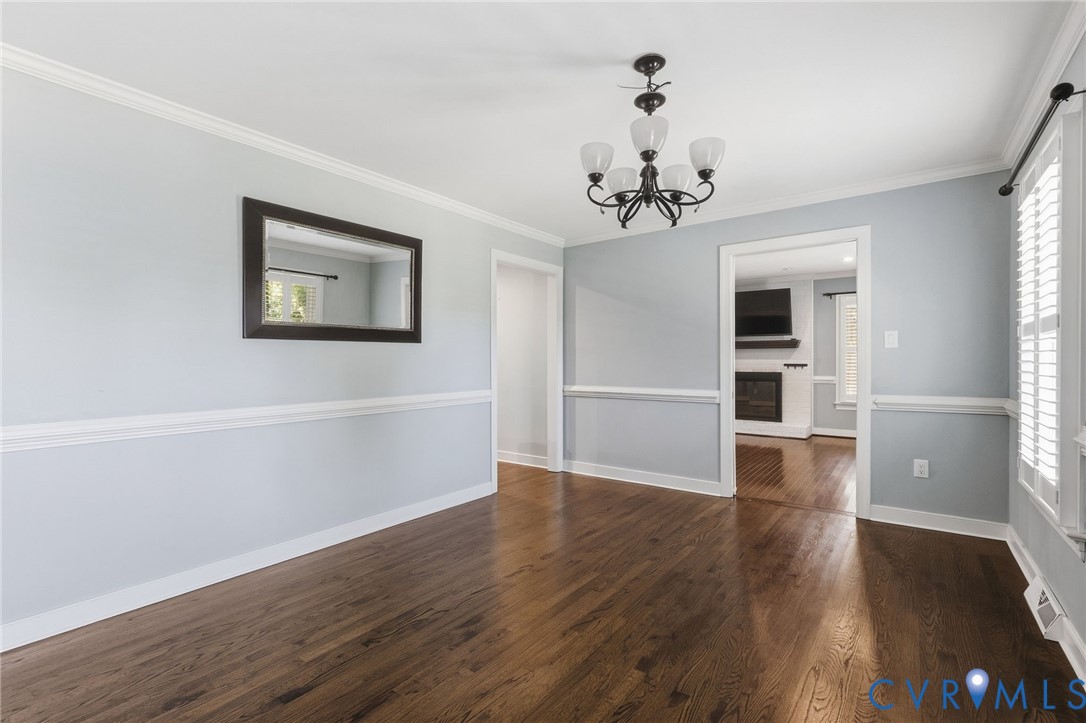 Room featuring wood-finish flooring, crown molding, chair rail trim, and an iron chandelier