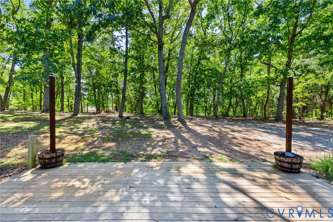 Ground-level wood deck featuring two decorative barrel planters and vertical wood posts, situated on a wooded lot with mature trees