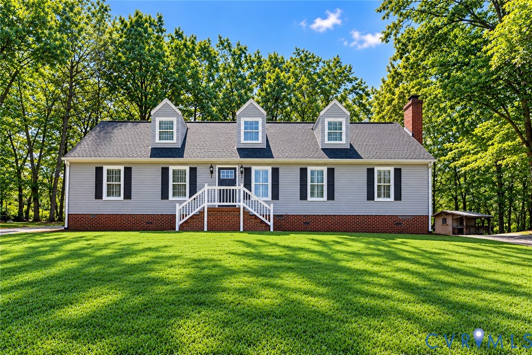 Cape Cod-style residence featuring horizontal siding, a red brick base, three roof dormers, and a masonry chimney Cape Cod-style residence featuring horizontal siding, a red brick base, three roof dormers, and a masonry chimney
