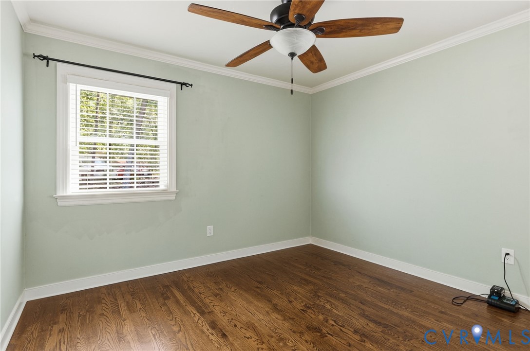 Room featuring wood-finish flooring, crown molding, a multi-blade ceiling fan with an integrated light fixture, and a window with horizontal blinds