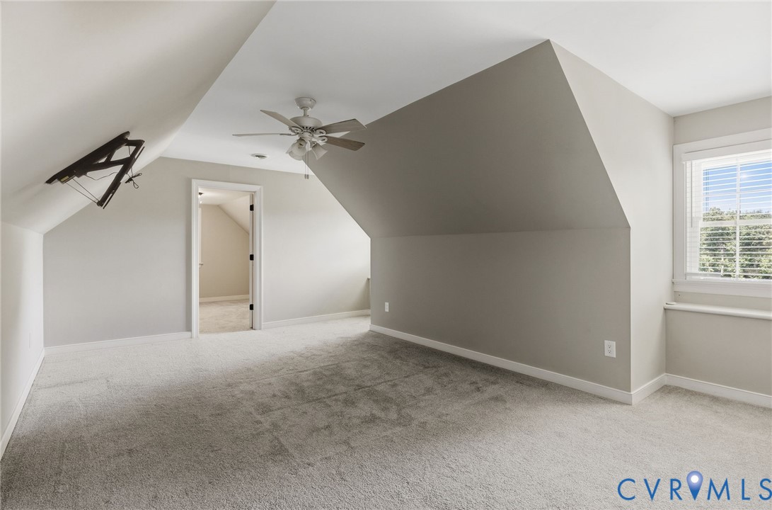 Upper-level space featuring vaulted ceilings, neutral wall tones, wall-to-wall carpeting, an attached ceiling fan with integrated lighting, and a window with blinds