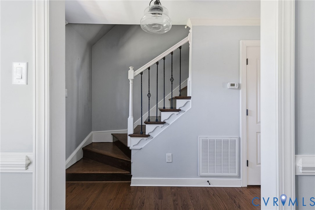 Staircase featuring dark wood-finish treads, decorative white millwork, and black metal balusters topped with a clear glass globe pendant light