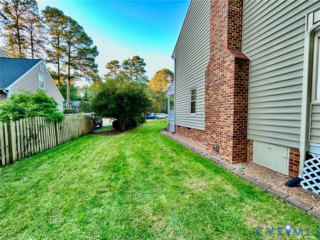 Exterior side yard featuring horizontal vinyl siding, a red brick chimney, a wood-slat privacy fence, and a stone-paver landscape border