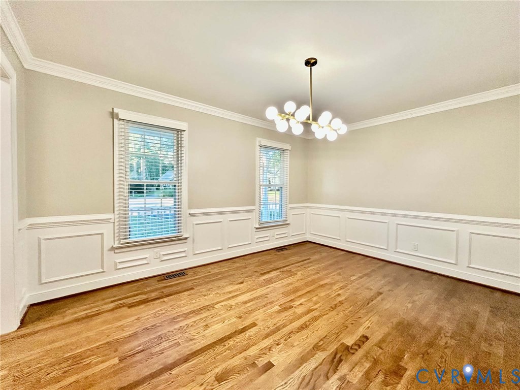 Dining space featuring wood-finish flooring, white wainscoting, crown molding, multi-light chandelier, and large windows with blinds