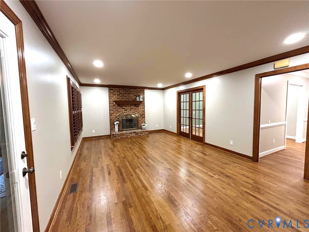 Hardwood flooring, brick fireplace with a mantel, crown molding, and French doors featuring multi-pane glass inserts